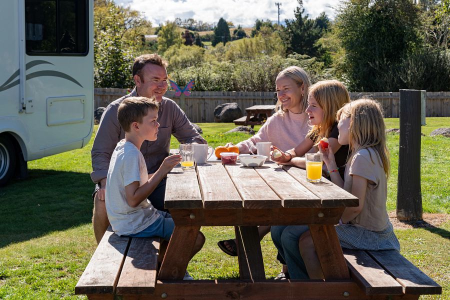 Gezin zit aan een picknicktafel op een camping in Nieuw-Zeeland