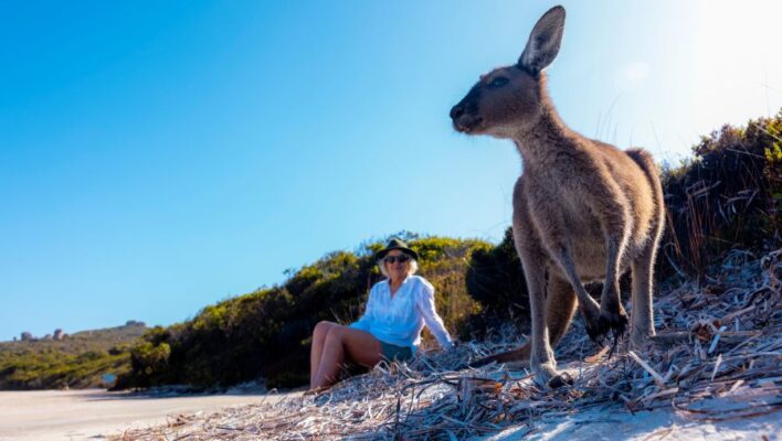 Vrouw zit bij Esperance op het Lucky Bay strand samen met een kangoeroe