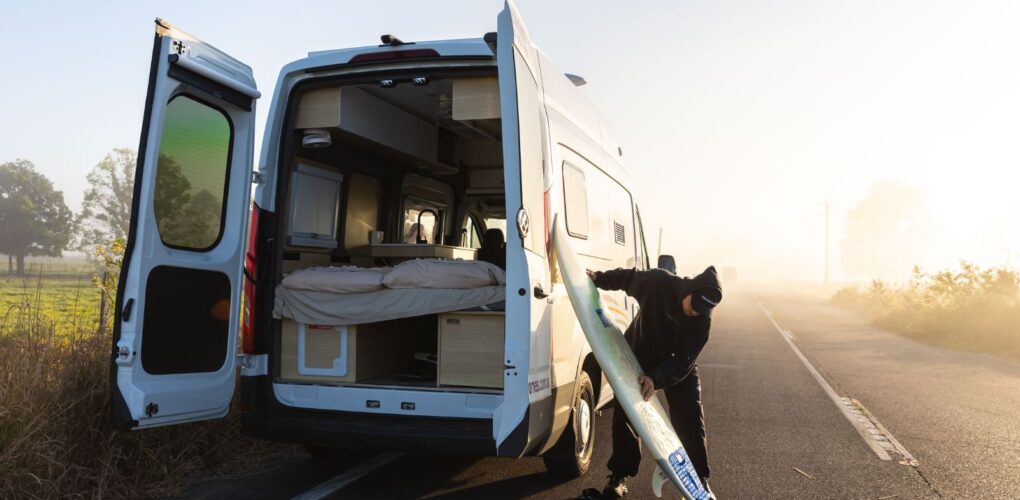 Cruisin' Rover staat geparkeerd met de achterdeuren open, man maakt surfplank klaar