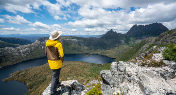 Man in gele regenjas kijkt uit over een meer in Cradle Mountain
