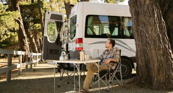 Man zit buiten aan de campingtafel bij een Mighty camper op een camping in Picton