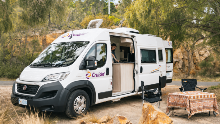 Zijaanzicht van de Cruisin' Sandpiper camper, vrouw staat in keuken binnen