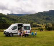 Gezin met jonge kinderen zit buiten aan tafel voor een Mighty Double Down camper