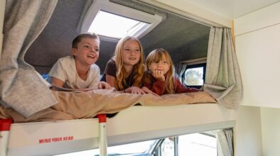 Drie kinderen liggen naast elkaar in de alkoof in de Apollo Euro Deluxe camper