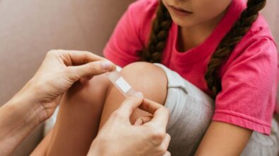 Moeder plakt pleister op kind van dochter met korte broek aan - goede ejhb doos mee is belangrijk