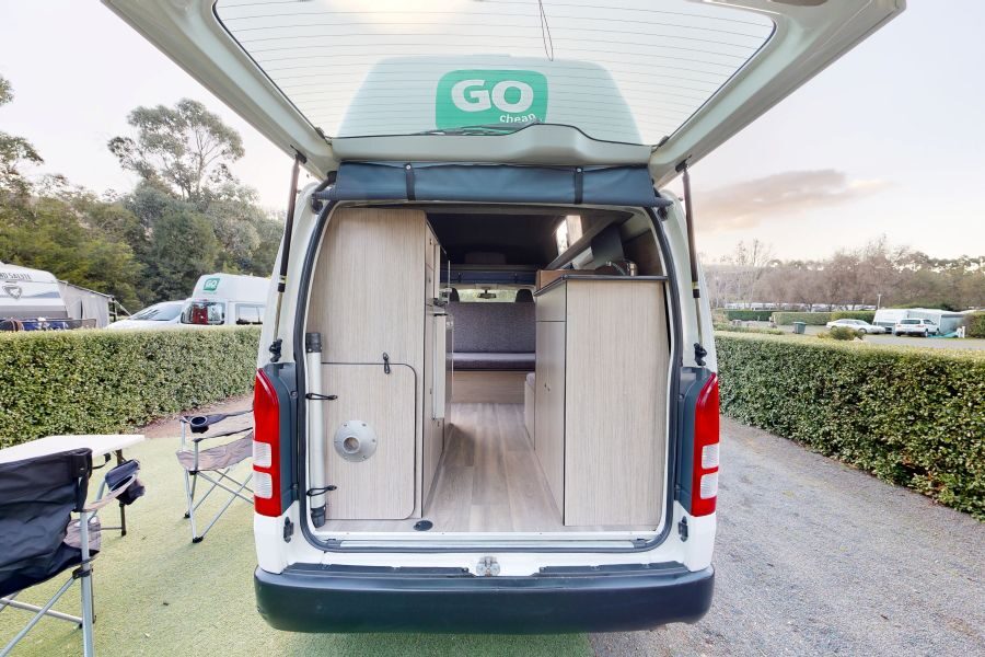 Zicht op het interieur van de Go Cheap 2 Berth Hitop, geparkeerd op een camping met de achterklep open en campingstoelen buiten