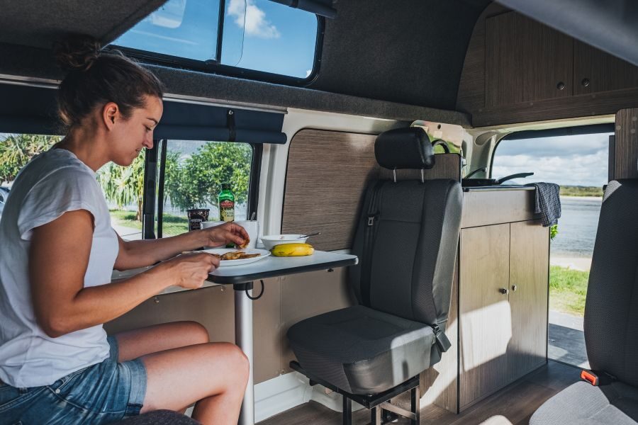 Een vrouw zit binnen aan de tafel van de Go Cheap 4 Berth Hitop