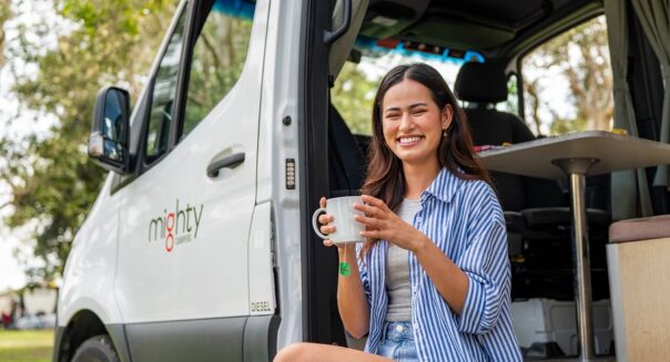 Vrouw geniet van kopje thee in de deuropening van de Mighty Deuce camper