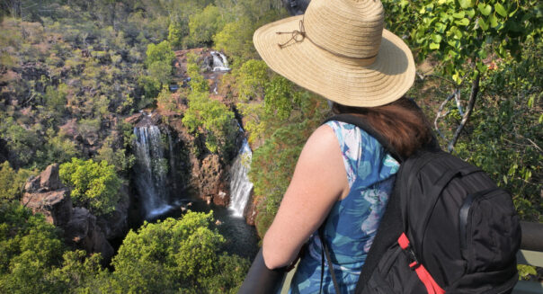 Vrouw met hoed op en rugzak op rug kijkt naar Florence Falls in Litchfield National Park