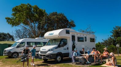 Gezin met Maui Beach camper zit buiten op de camping, twee tieners komen aanlopen met nog meer stoelen