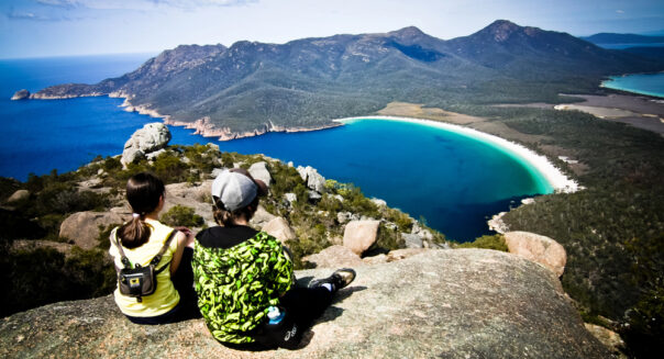 Twee mensen zitten op een rots en kijken uit over Wineglass Bay in Freycinet National Park