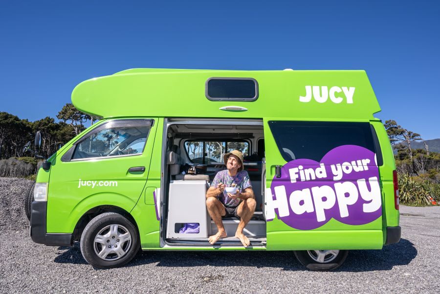 Man eet zittend uit een bakje in de zijdeur van de Jucy Chaser