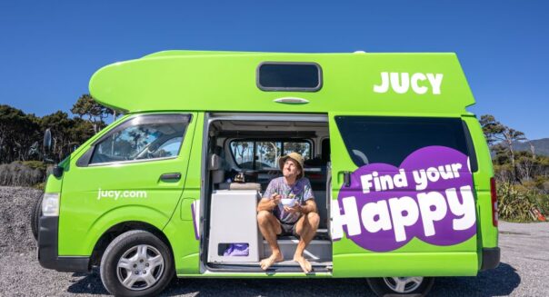 Man eet zittend uit een bakje in de zijdeur van de Jucy Chaser