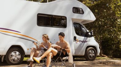 Koppel zit in campingstoelen voor de Cruisin' Seeker camper en is aan het lunchen
