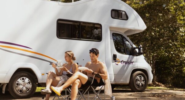 Koppel zit in campingstoelen voor de Cruisin' Seeker camper en is aan het lunchen