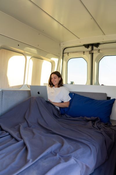 Vrouw is bezig op haar laptop in het opgemaakte bed van de Jucy Coaster
