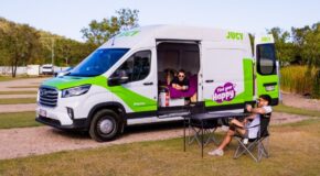 Jucy Coaster staat op een camping met de zij- en achterdeuren open, een man ligt op het bed en een man zit op een campingstoel buiten