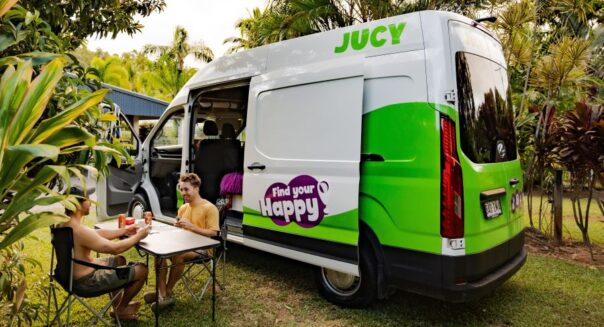 Jucy Coaster staat op een campingplaats met de voor, - en zijdeur open, twee mannen zitten buiten aan tafel
