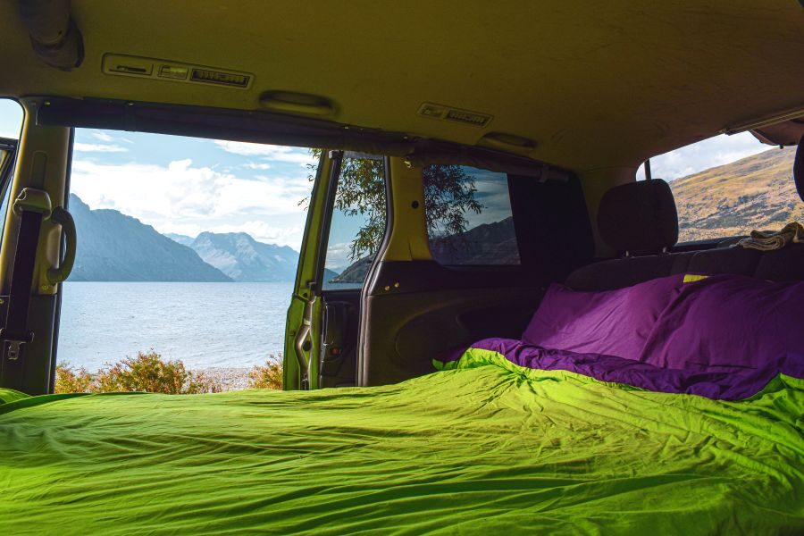 Zicht op een meer met bergen vanuit het opgemaakte bed van de Jucy Crib