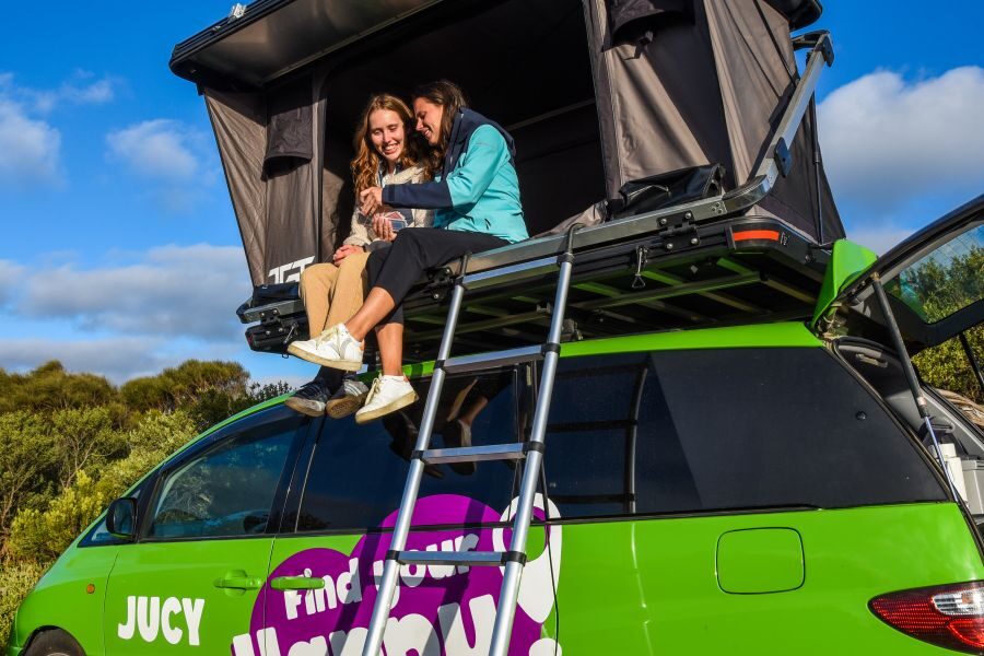 Twee vrouwen zitten in de daktent van de Jucy Crib Plus