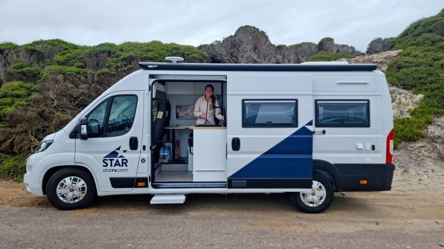 Zijaanzicht van de Star RV Polaris 2, schuifdeur is open en een vrouw maakt gebruik van de keuken