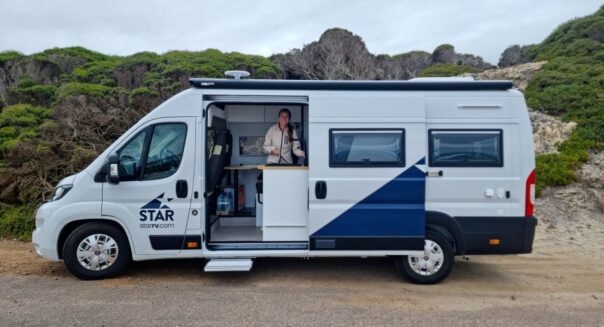 Zijaanzicht van de Star RV Polaris 2, schuifdeur is open en een vrouw maakt gebruik van de keuken