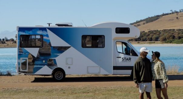 Een stel staat voor de Star RV Polaris 6 die geparkeerd staat aan het water