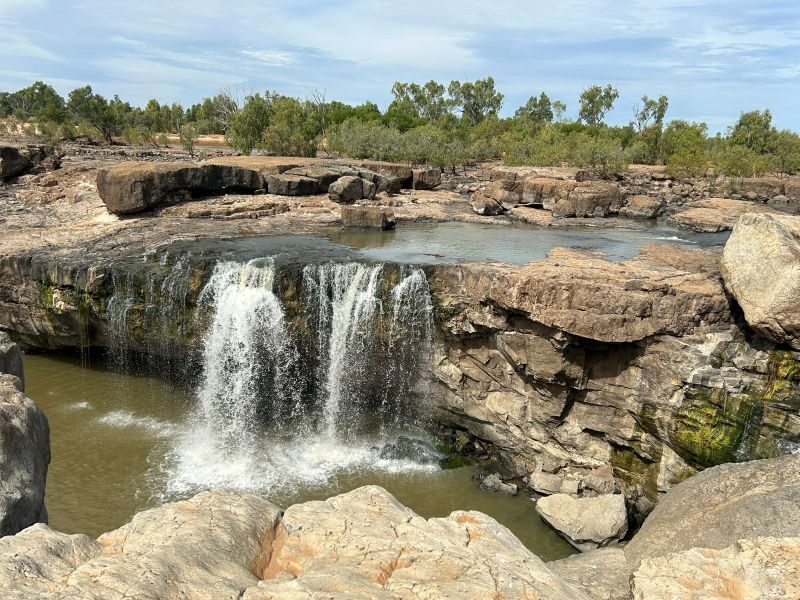 Brede rotsplaten en een waterval die uit de rivier naar beneden valt in de Leichhardt Falls