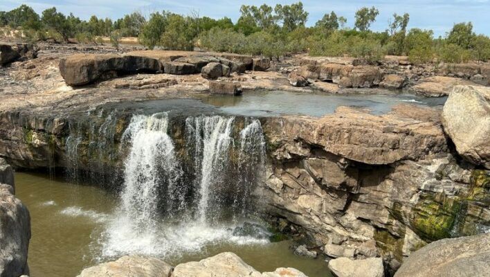 Brede rotsplaten en een waterval die uit de rivier naar beneden valt in de Leichhardt Falls