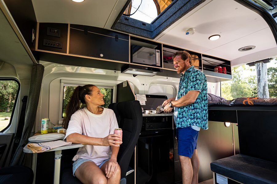 Apollo Endeavour interieur met ingang naar pop up roof top tent vanuit binnen en koppel in de camper aan het koken