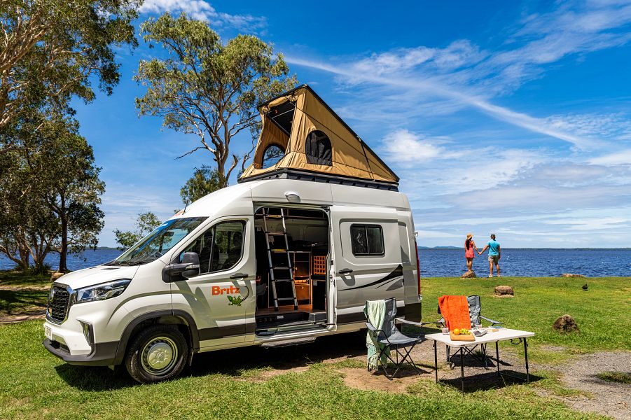 Britz Voyager camper staat geparkeerd met daktent omhoog, schuifdeur open en campingset ervoor