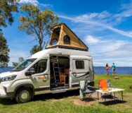 Britz Voyager camper staat geparkeerd met daktent omhoog, schuifdeur open en campingset ervoor