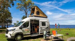 Britz Voyager camper staat geparkeerd met daktent omhoog, schuifdeur open en campingset ervoor