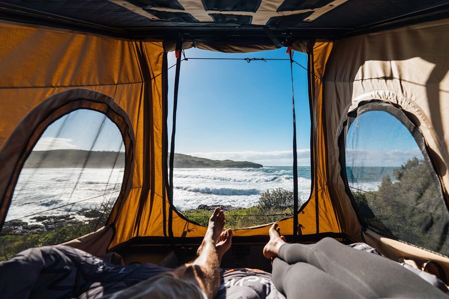 Britz Voyager Australië binnenkant pop up rooftop tent waar een stel in bed ligt met uitzicht op zee