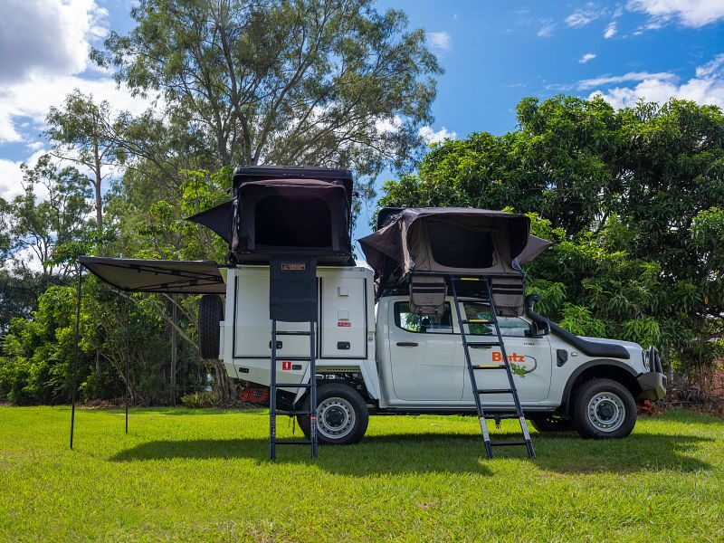 Britz Warrior 4WD staat geparkeerd op het gras met daktenten en luifel uitgeklapt