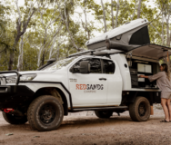 De vrouwelijke camperreiziger is bezig een maaltijd te bereiden in het keukengedeelte aan de zijkant van de RedSands 4WD camper