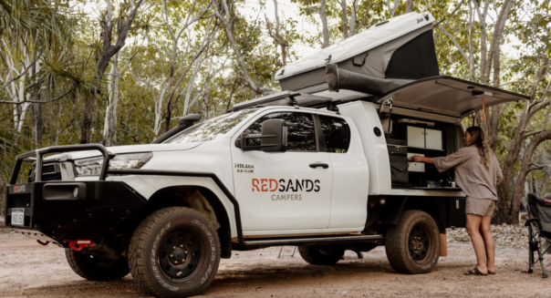 De vrouwelijke camperreiziger is bezig een maaltijd te bereiden in het keukengedeelte aan de zijkant van de RedSands 4WD camper