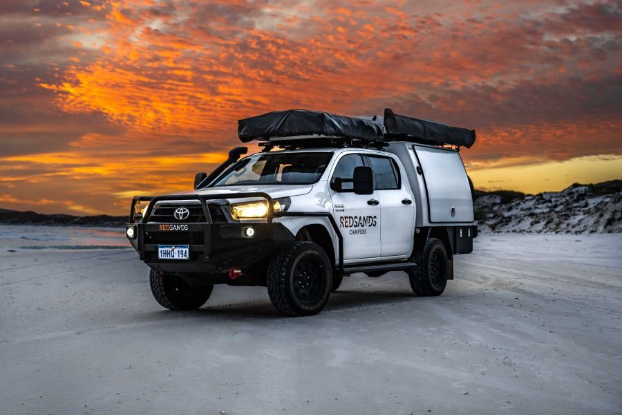 De robuuste RedSands 4WD met twee daktenten staat geparkeerd op het strand bij een kleurrijke zonsondergang
