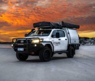 De robuuste RedSands 4WD met twee daktenten staat geparkeerd op het strand bij een kleurrijke zonsondergang