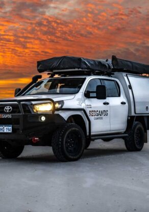De robuuste RedSands 4WD met twee daktenten staat geparkeerd op het strand bij een kleurrijke zonsondergang