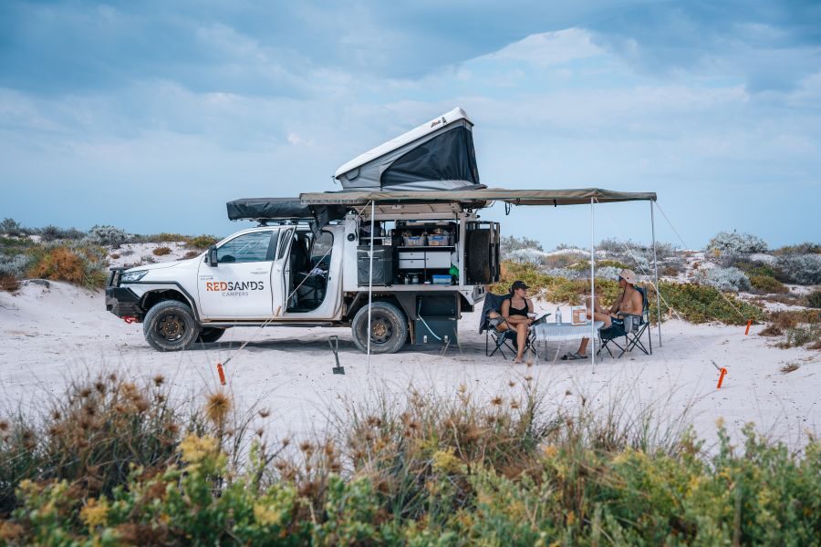 De reizigers hebben een prachtige locatie gevonden om te kamperen bij Coral Bay - West Australië - met zicht op de zijkant van de RedSands camper en opengeklapte daktent