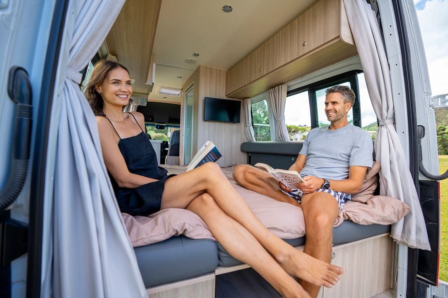 Een koppel zit achterin de Britz Venturer camper op het bed een boek te lezen met de achterdeuren open