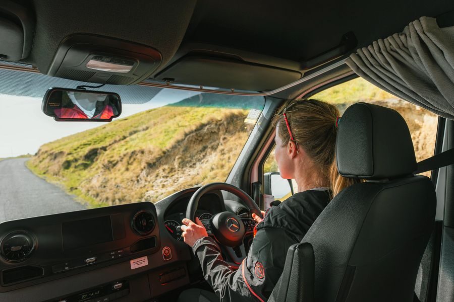 Een vrouw zit op de bestuurderstoel en is aan het rijden in de Britz Venturer camper door Nieuw-Zeeland