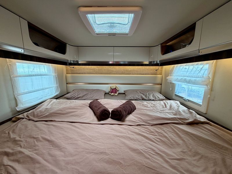 Een opgemaakt tweepersoonsbed met kastruimte erboven achterin de Britz Wanderer camper in Nieuw-Zeeland