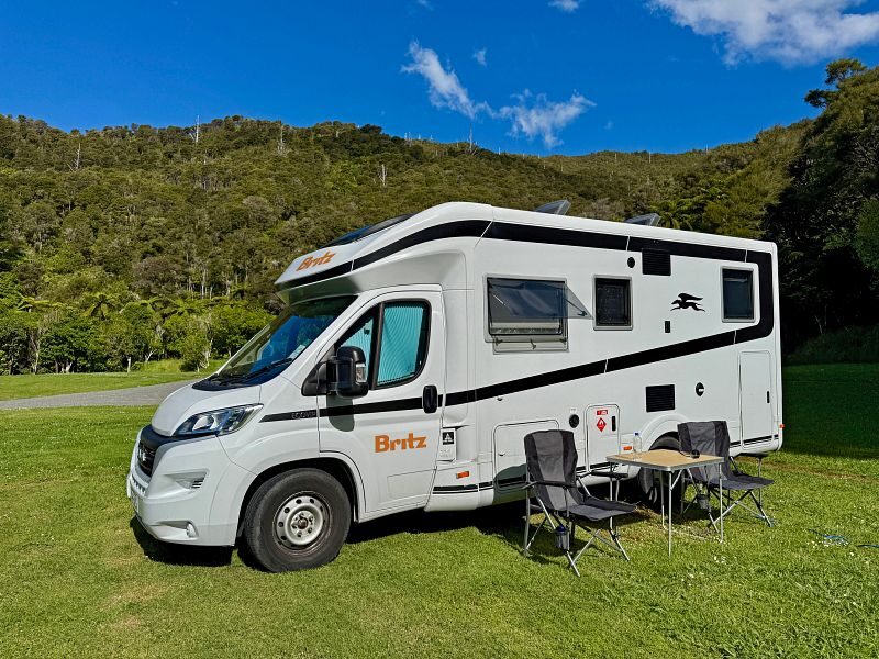 De Britz Wanderer staat geparkeerd op een grasveld in Nieuw-Zeeland met twee stoelen en een tafel voor de camper