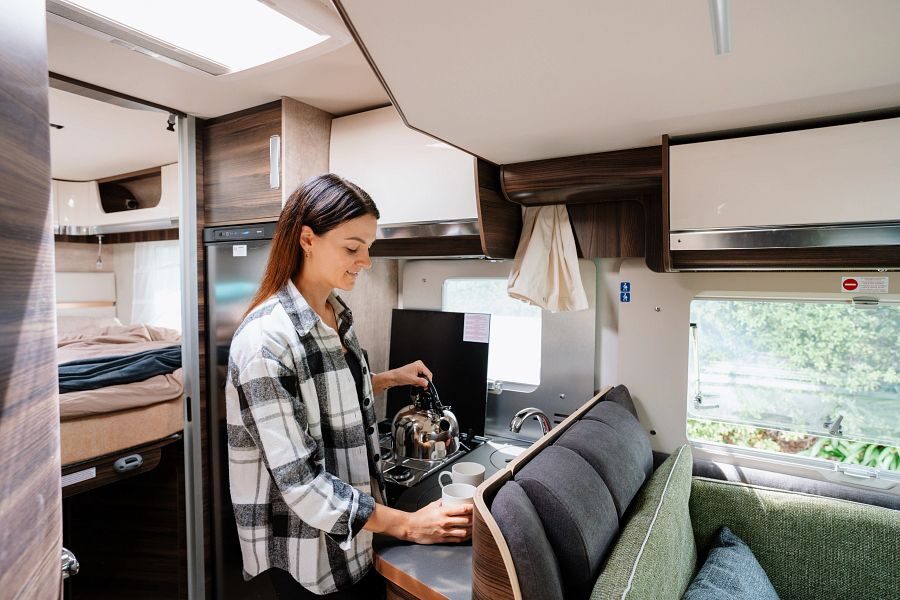 Een vrouw schenkt drinken in een mok in de keuken van de Britz Wanderer camper in Nieuw-Zeeland
