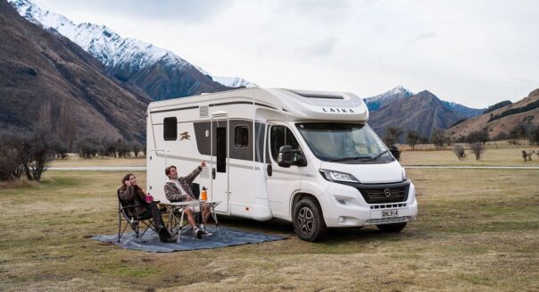 Koppel zit op de campingstoelen aan tafel buiten de Britz Odyssey camper in de bergen van Nieuw-Zeeland