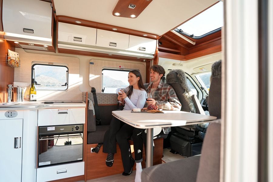 Een koppel zit op het bankje aan tafel voorin de Britz Odyssey camper naast de keuken in Nieuw-Zeeland