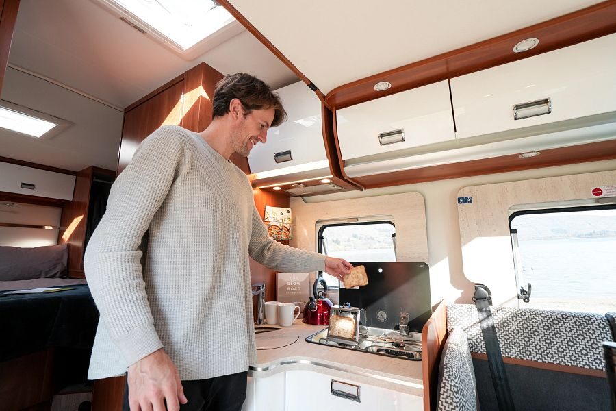 Een man is brood aan het roosteren in de keuken van de Britz Odyssey camper in Nieuw-Zeeland