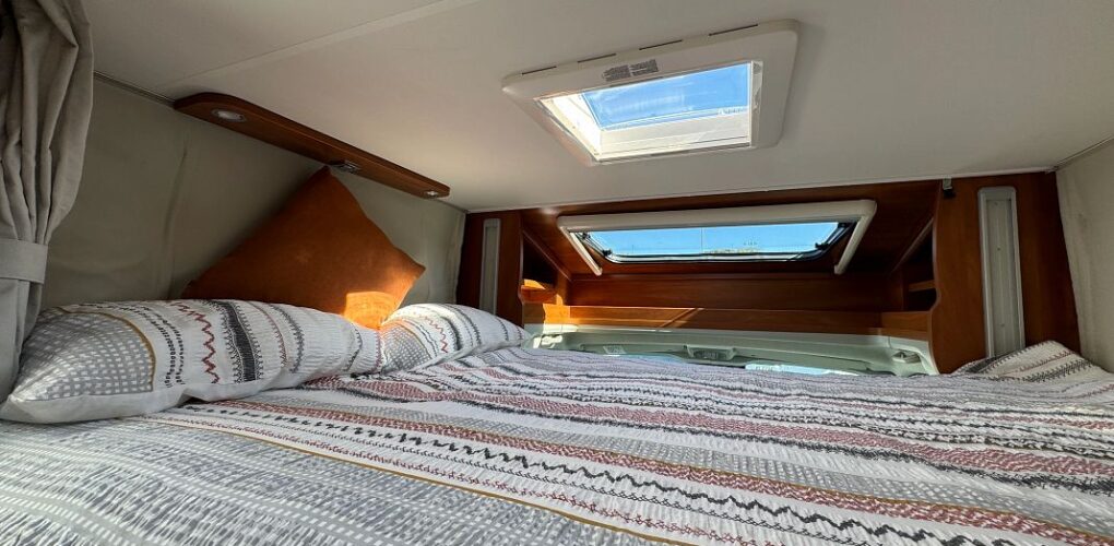 Een opgemaakt tweepersoonsbed boven in de Britz Odyssey camper met dakraam